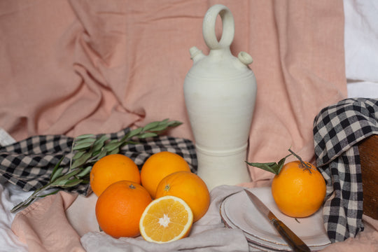 bodegón de naranjas con botijo, mantel de cuadros, plato y cuchillo
